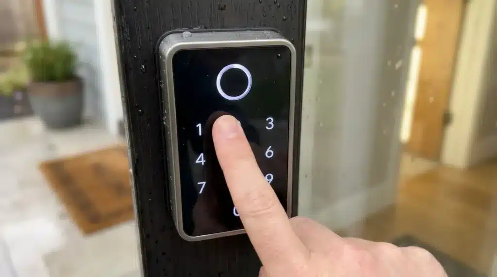 Person entering a PIN code on a backlit keyless digital door lock keypad on a front door